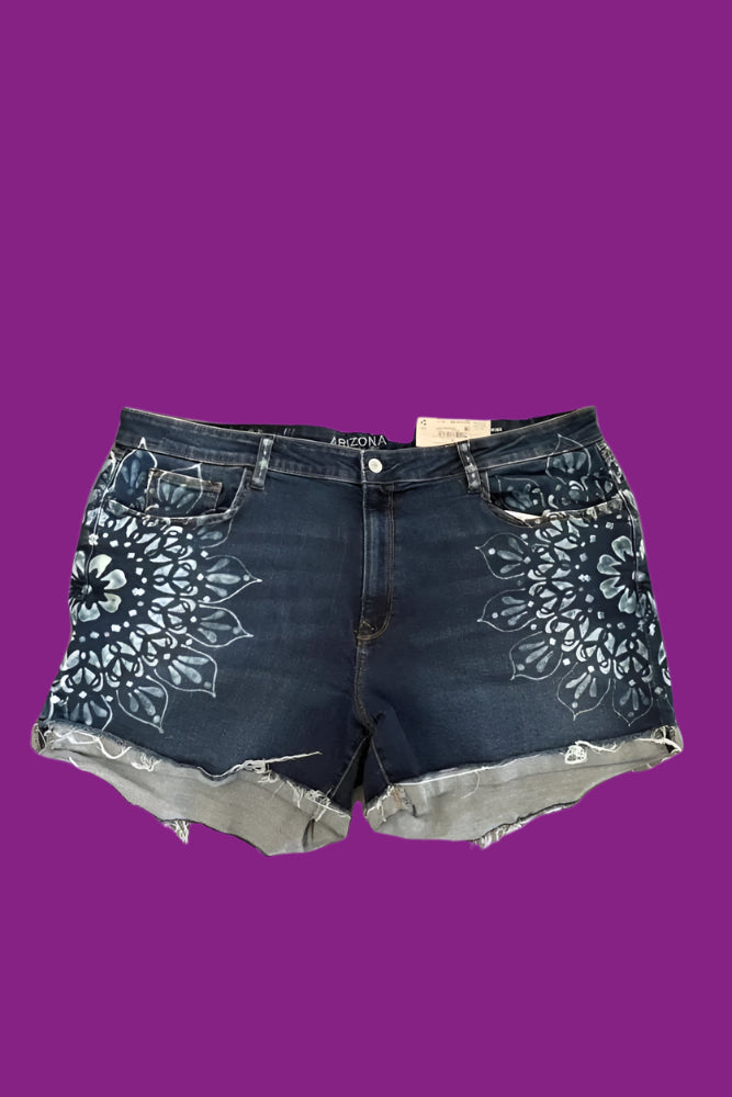 A pair of blue denim shorts with hand dyed mandalas on the front and back, and dotted details on belt loops, presented on a plain background.